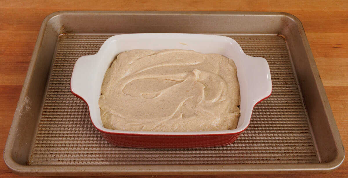 spice cake batter in a small baking dish on a rimmed baking sheet.