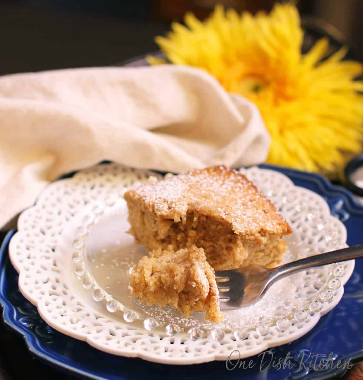 A square piece of spice cake dusted with powdered sugar on a small plate with a fork.