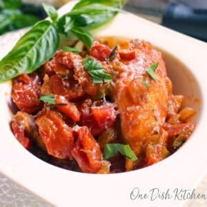 single serving chicken cacciatore with fresh basil in a white bowl.