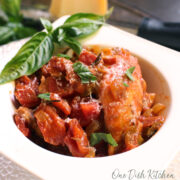 chicken cacciatore in a white bowl topped with a large sprig of fresh basil