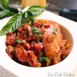 chicken cacciatore in a white bowl topped with a large sprig of fresh basil