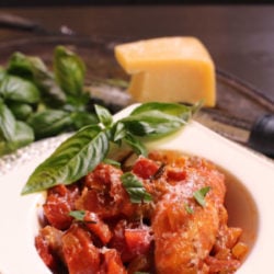 a bowl of chicken cacciatore on a silver tray next to a wedge of parmesan cheese.