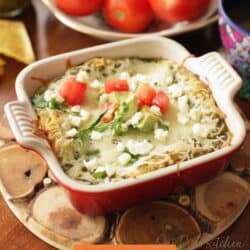 layered chicken enchiladas in a small red baking dish.
