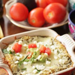 enchiladas verdes on a table surrounded by tomatoes and jars of salsa.
