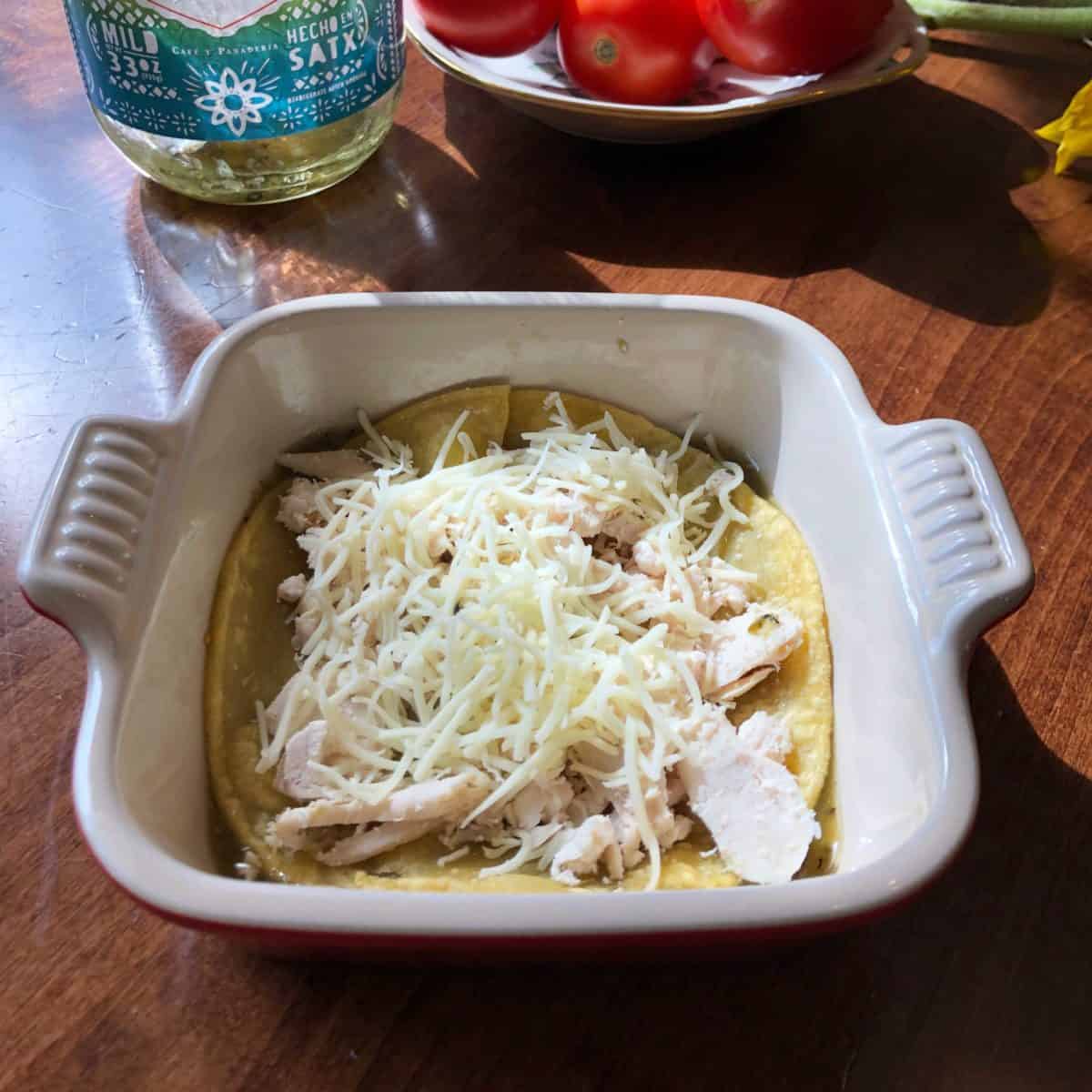 a corn tortilla in a small dish topped with chicken and cheese.
