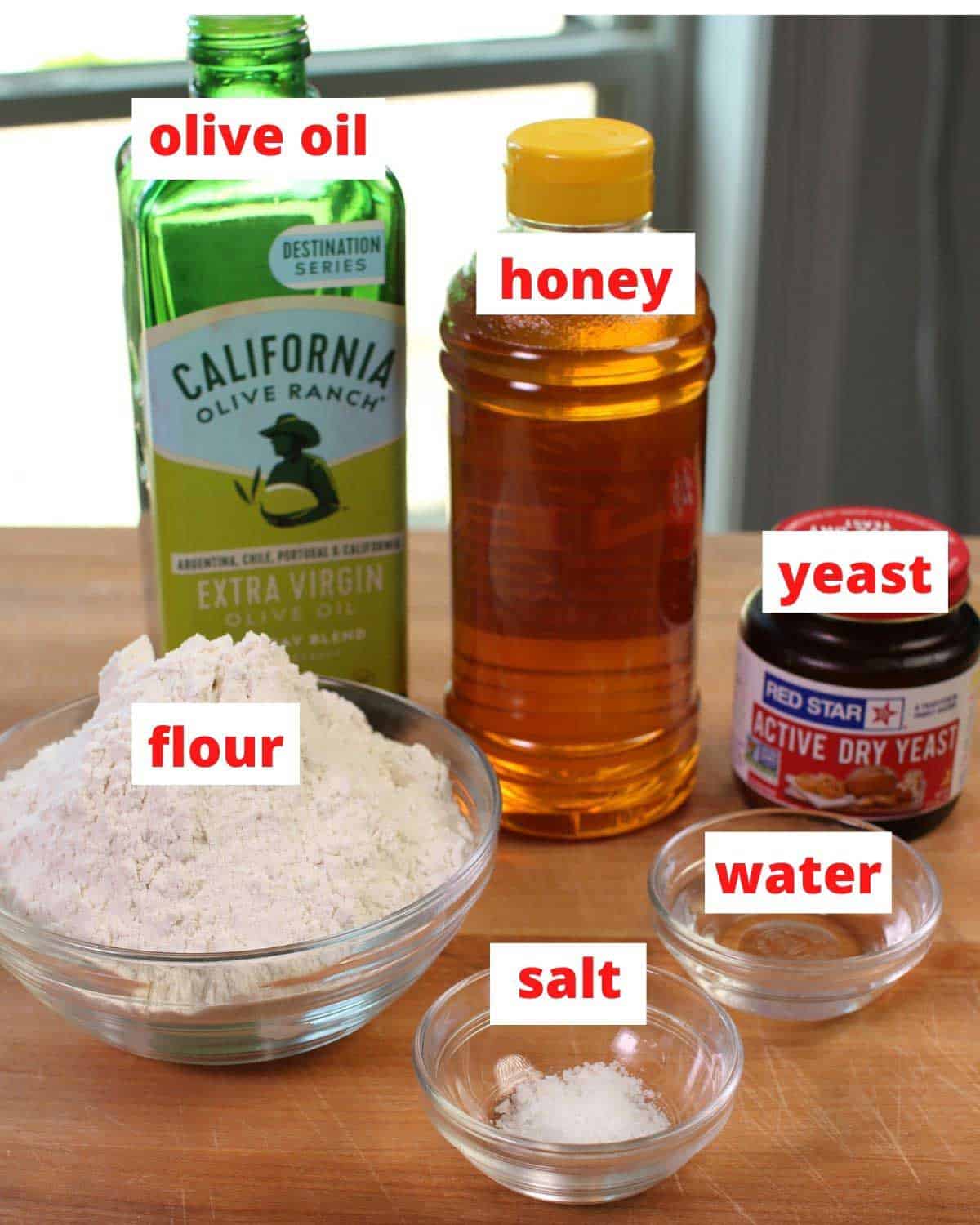 ingredients needed to make french bread including flour, yeast, and water on a wooden table.