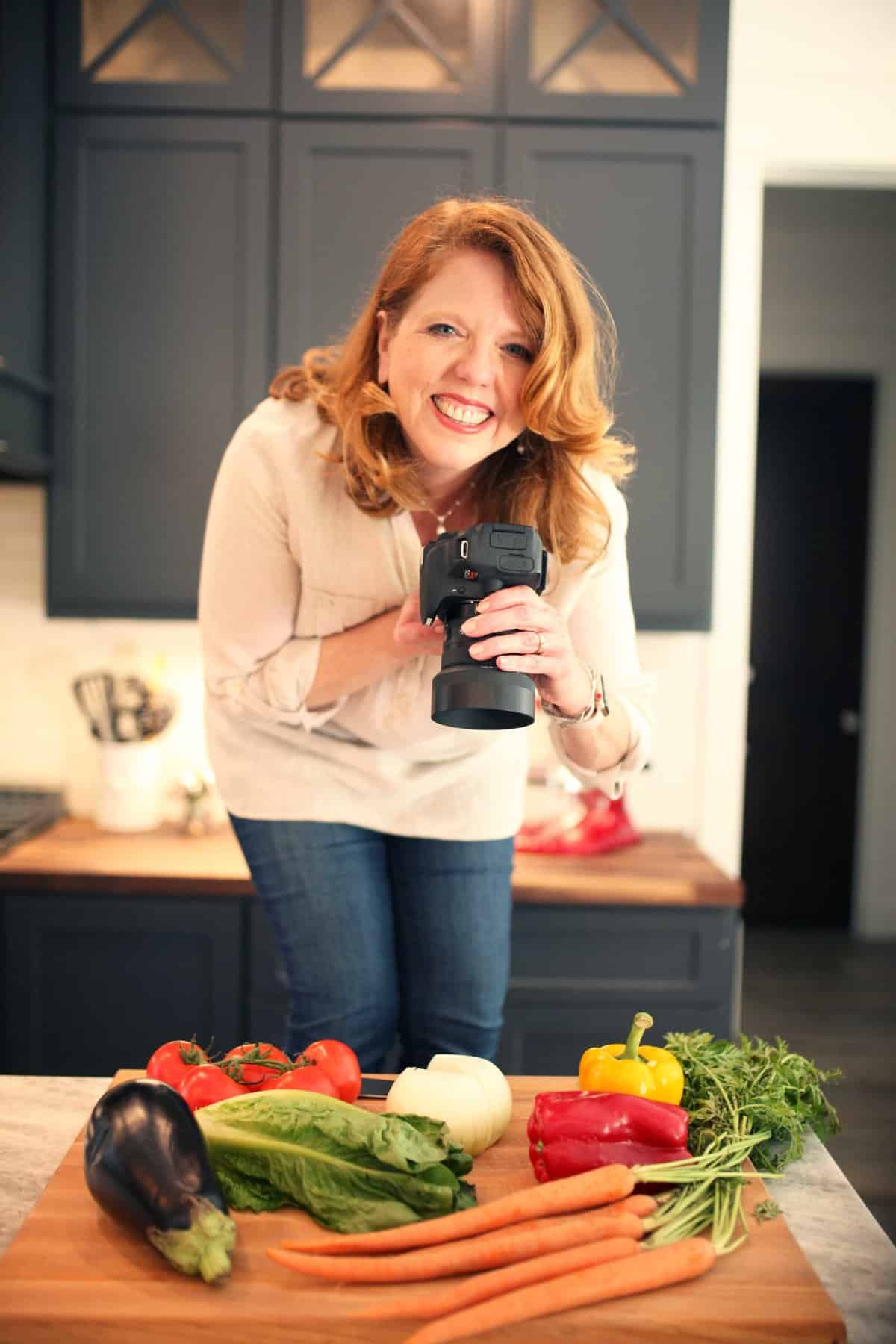 joanie smiling with camera in hand standing above vegetables.