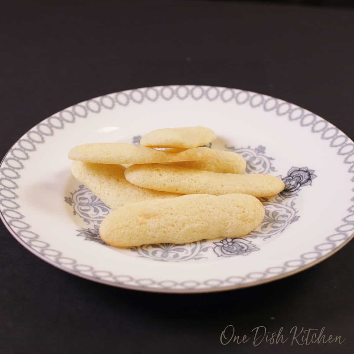 Five ladyfingers on a white plate.