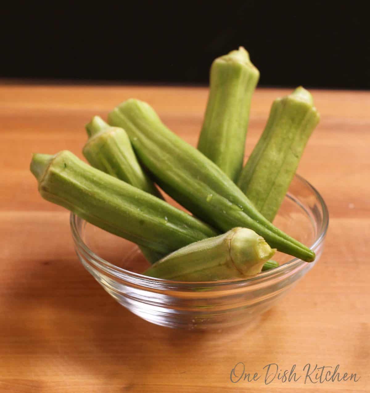 A small bowl of fresh okra on a cutting board.