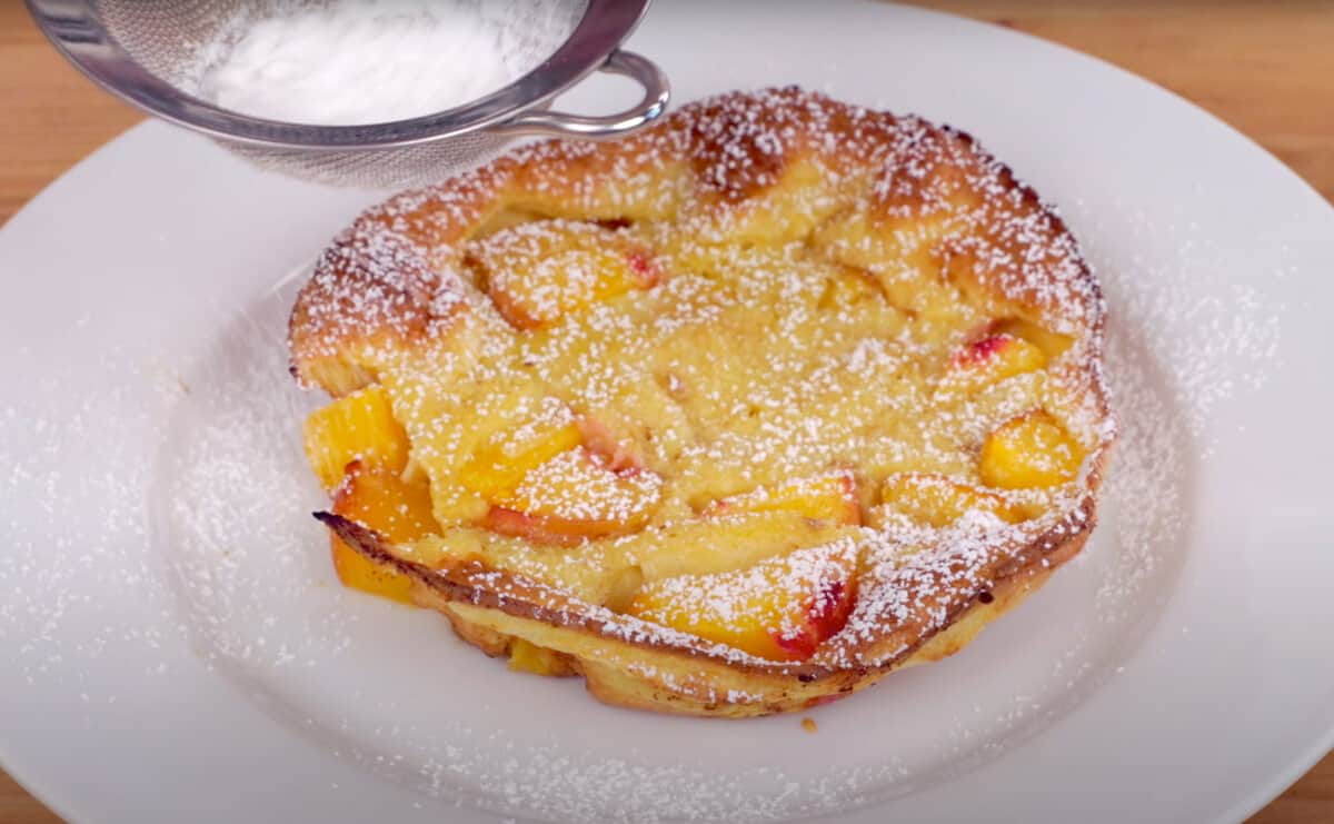 a peach filled dutch baby on a plate with a topping of powdered sugar