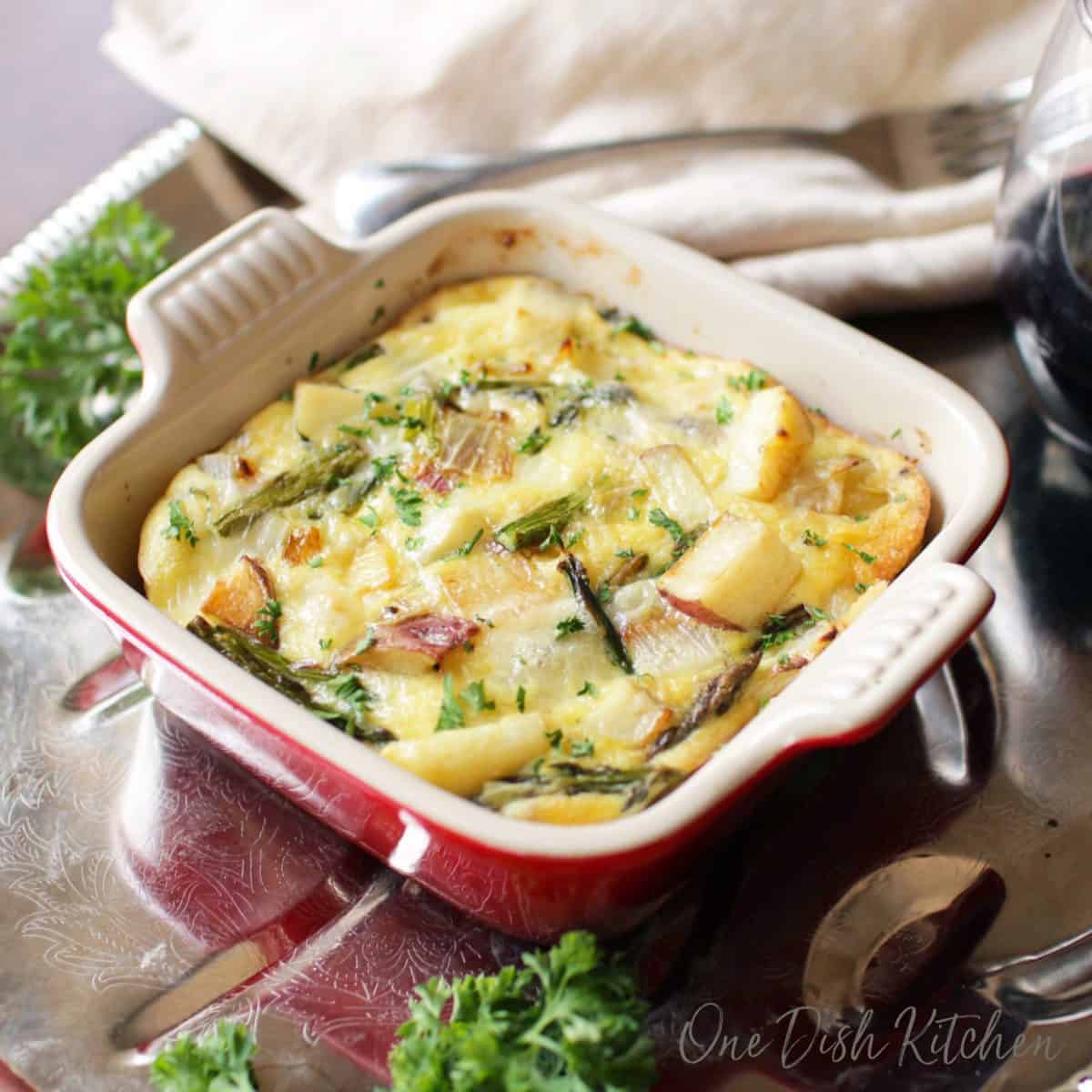 a quiche in a small red baking dish on a silver tray.