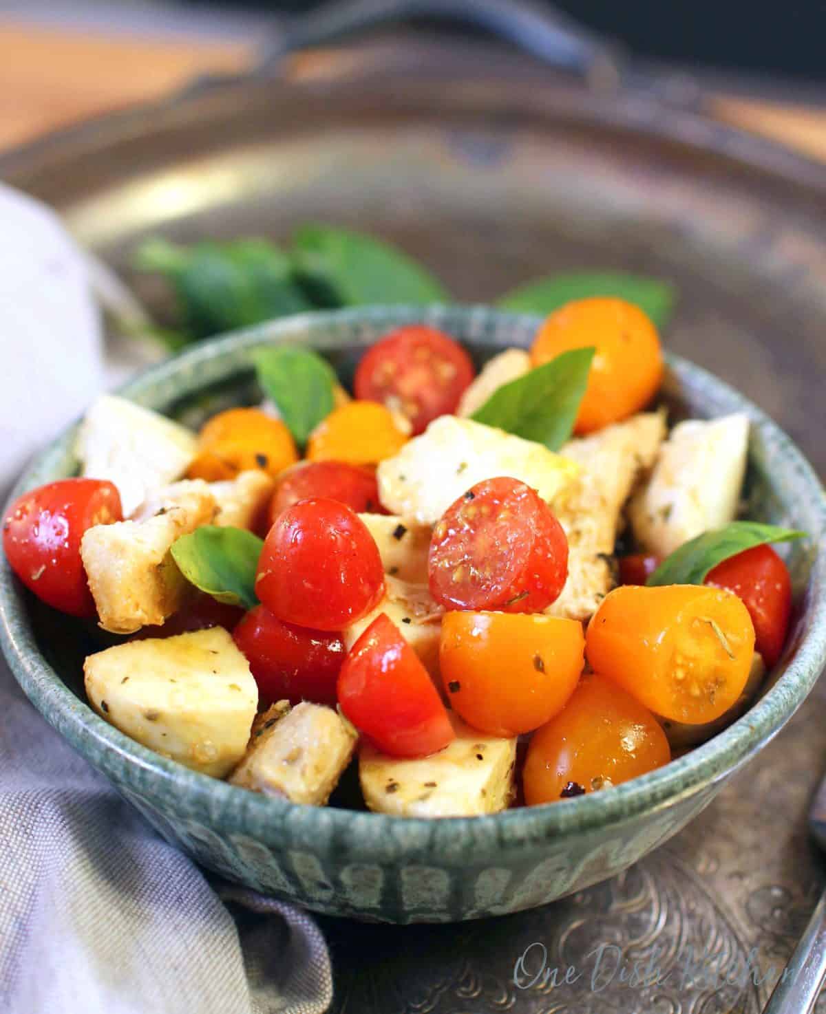 a blue bowl filled with cooked chicken, red and yellow tomatoes, and fresh basil.