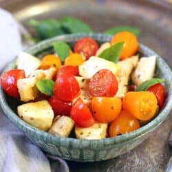 a blue bowl filled with cooked chicken, red and yellow tomatoes, and fresh basil.