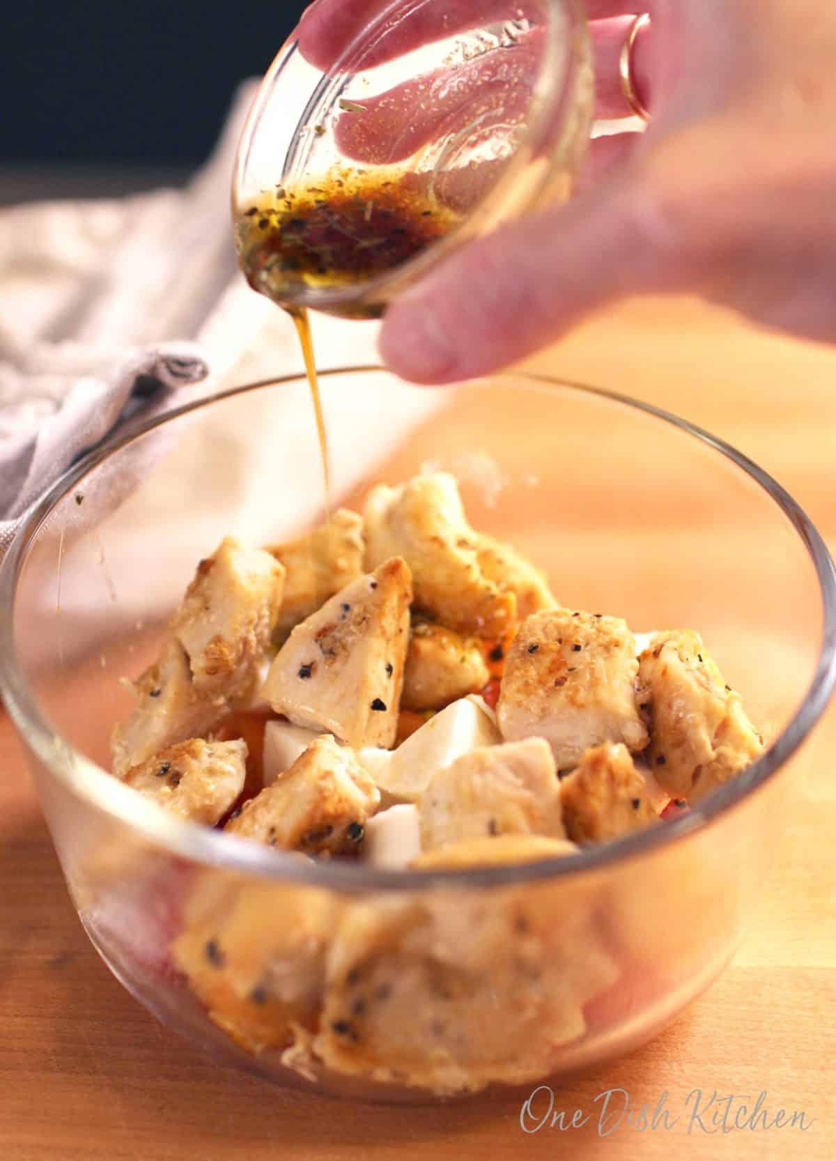 pouring dressing over chopped chicken in a bowl.