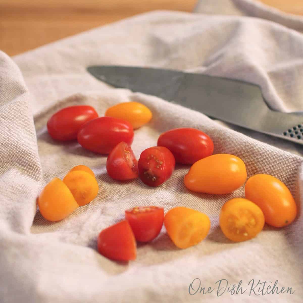 a scattering of red and yellow cherry tomatoes on a tan colored napkin next to a sharp knife.