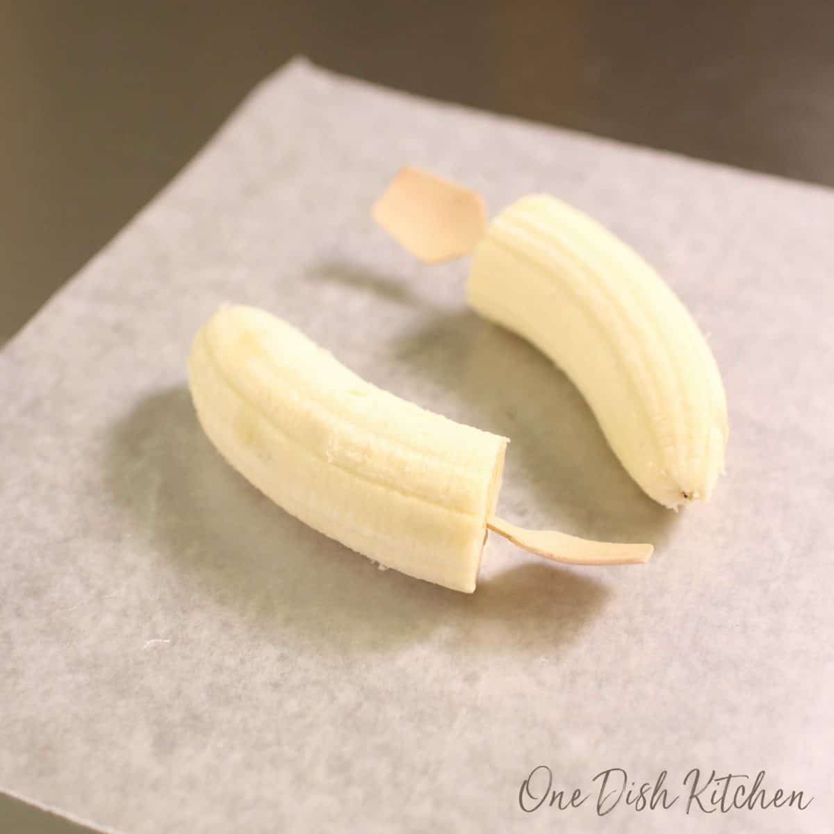 two bananas on a piece of wax paper with a wooden spoon stuck in each end.
