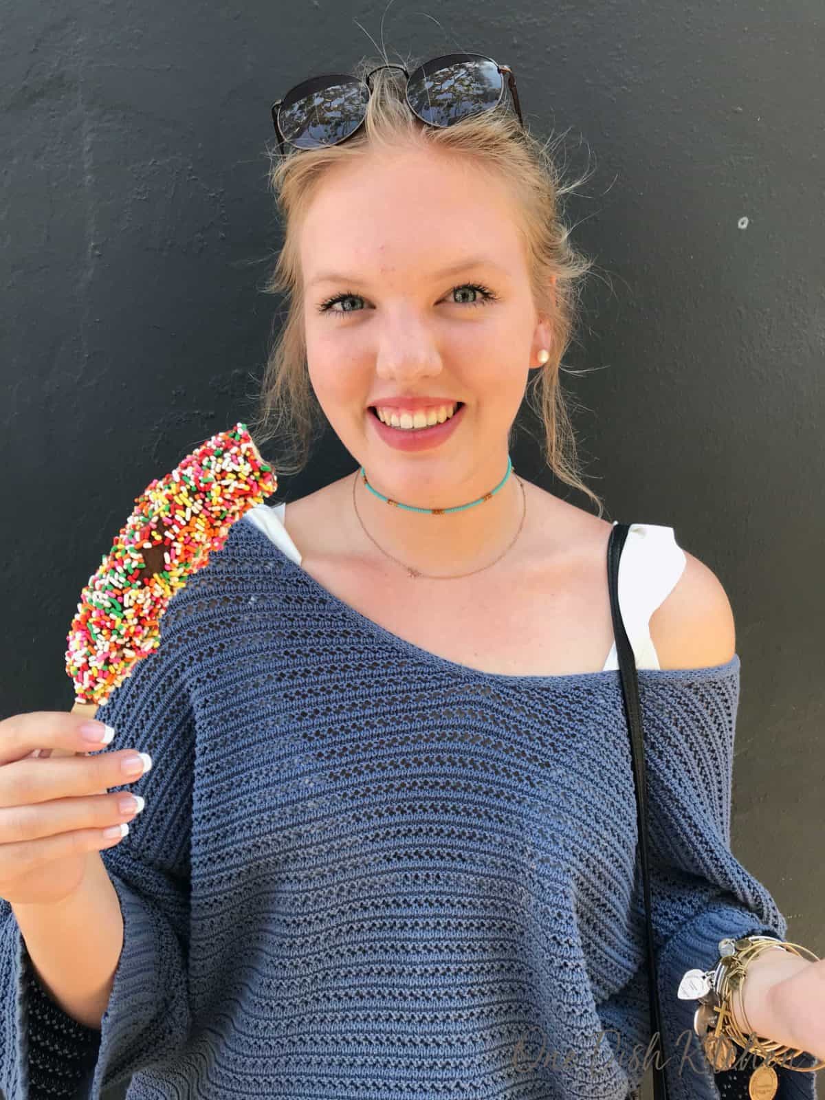 a girl holding a frozen chocolate bananas dipped in sprinkles.
