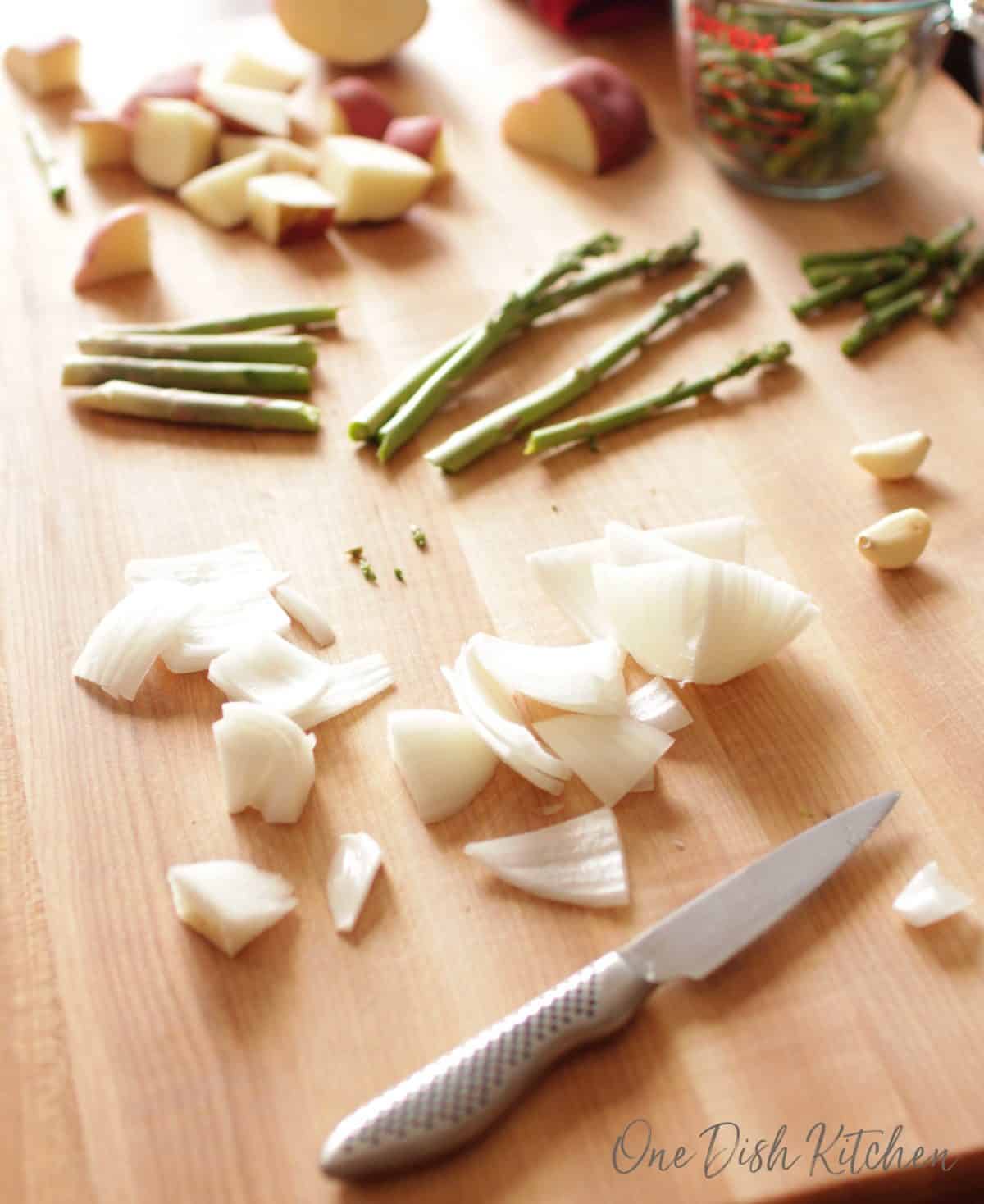 a cutting board with a small knife and cut asparagus, potatoes, and garlic scattered on the board.
