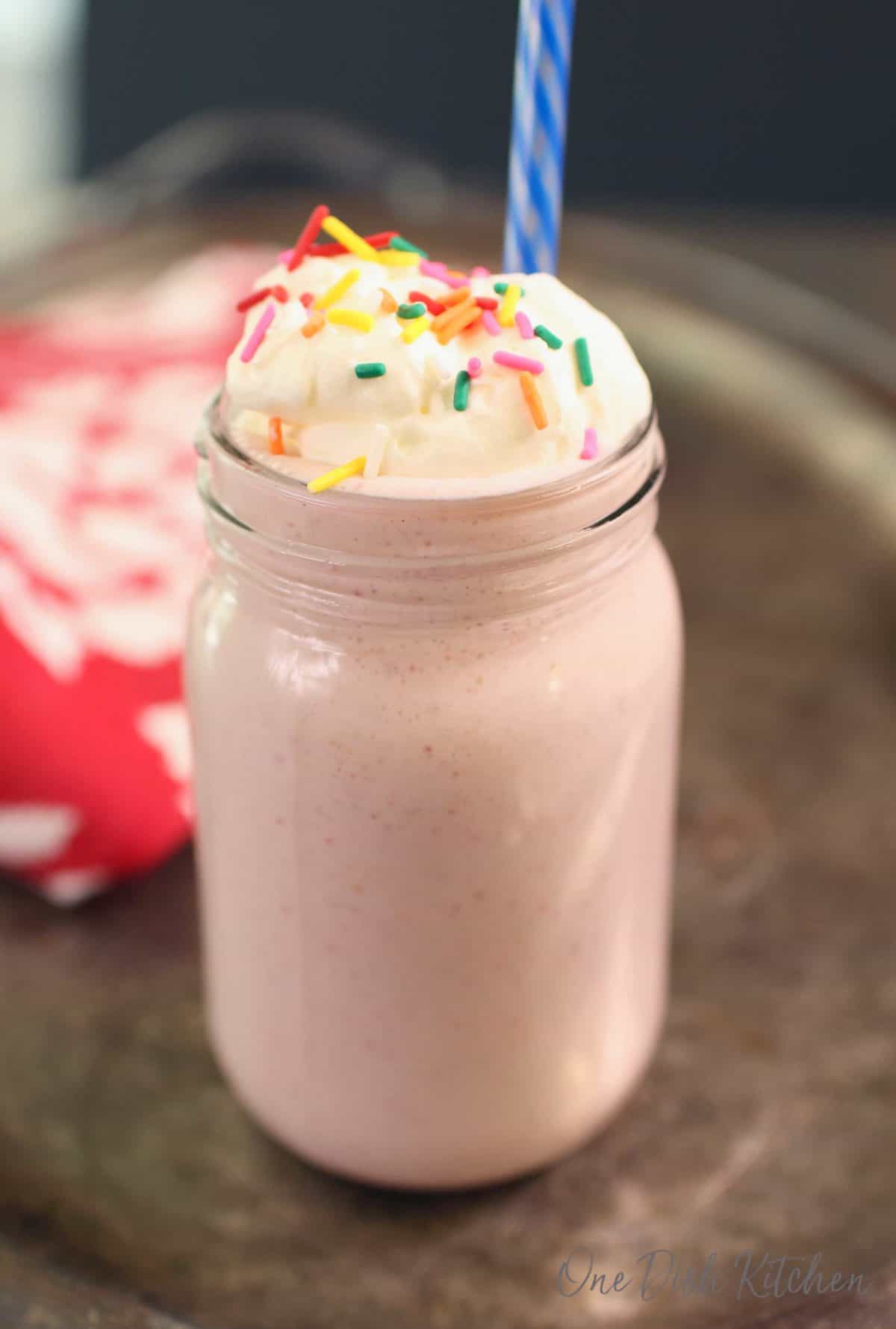 a milkshake in a tall clear glass topped with whipped cream and colored sprinkles.