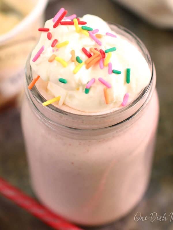 a single strawberry milkshake topped with whipped cream and sprinkles.