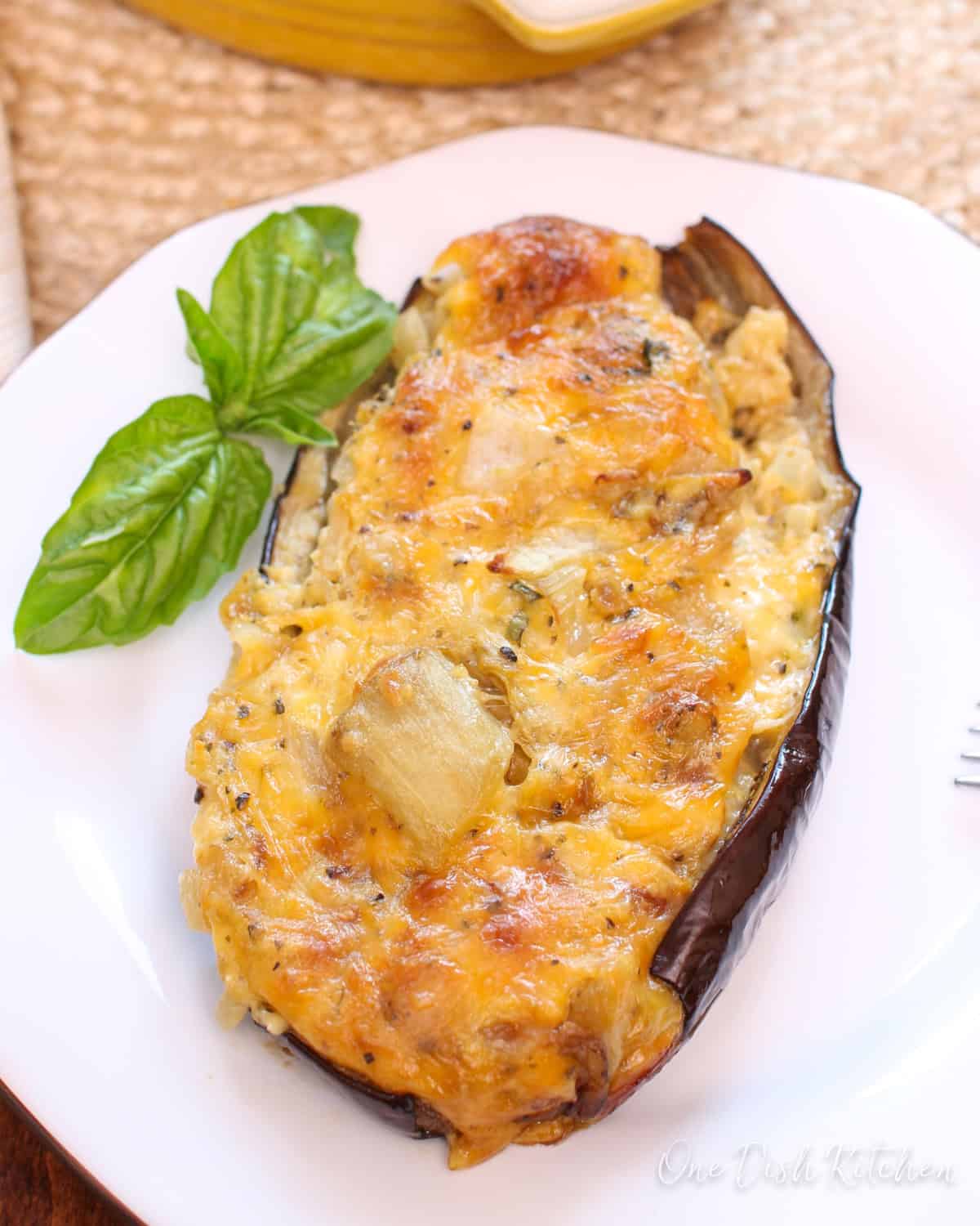 a baked stuffed eggplant topped with cheese on a white plate.
