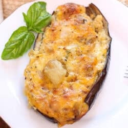 a baked stuffed eggplant topped with cheese on a white plate.