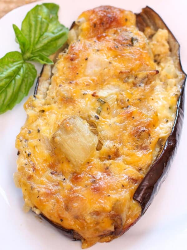 a baked stuffed eggplant topped with cheese on a white plate.