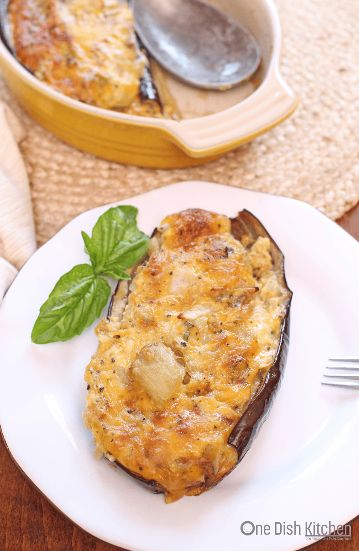 twice baked eggplant on white plate with basil leaf.