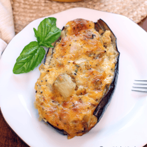 half of twice baked eggplant one a white plate with basil leaves.