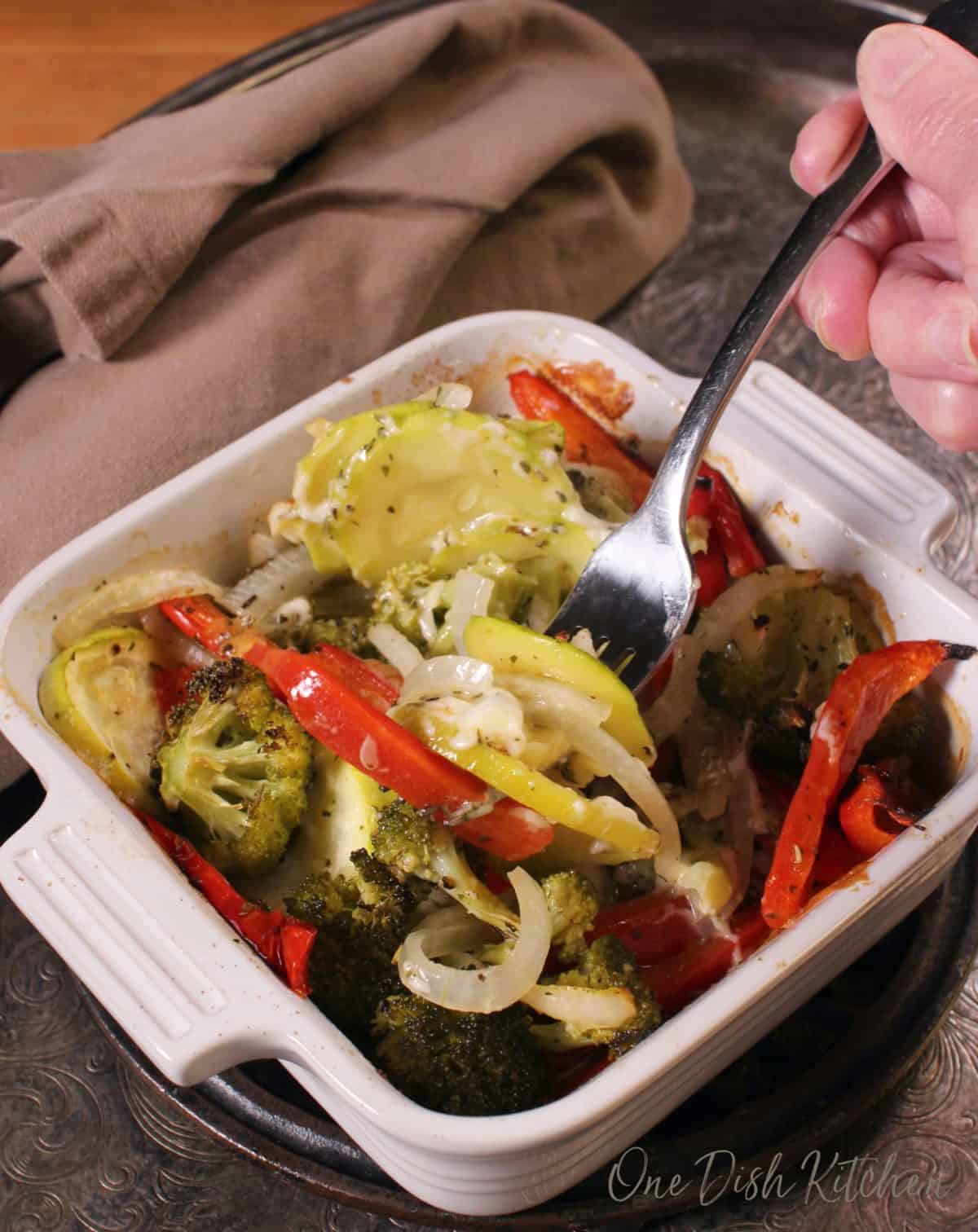 a forkful of vegetables being eaten out of a white casserole dish.