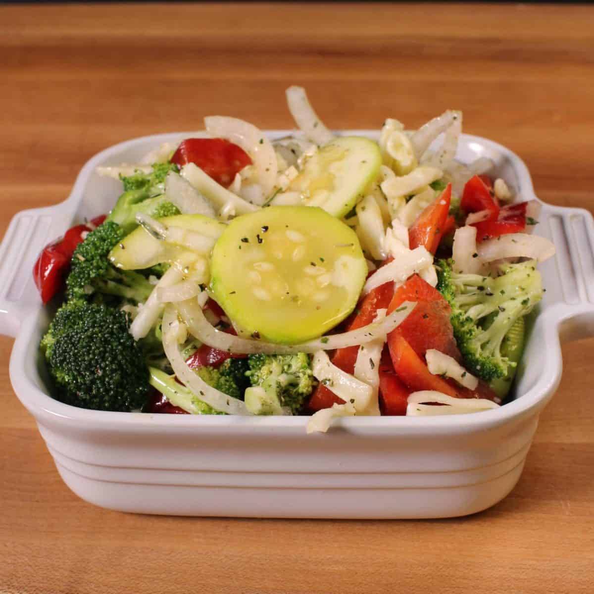 onions, zucchini and red peppers in a small white baking dish.