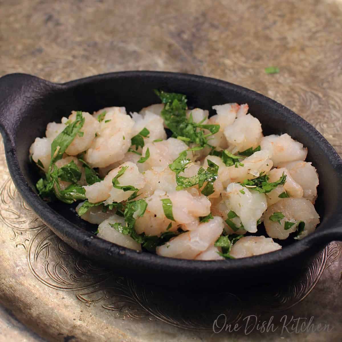 raw shrimp topped with chopped parsley in a baking dish.