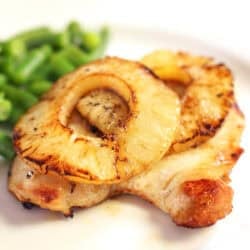 a broiled chicken breast topped with a charred pineapple slice and served with green beans.
