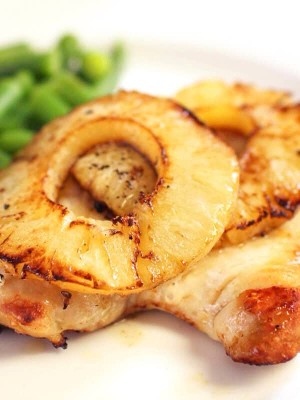 a broiled chicken breast topped with a charred pineapple slice and served with green beans.