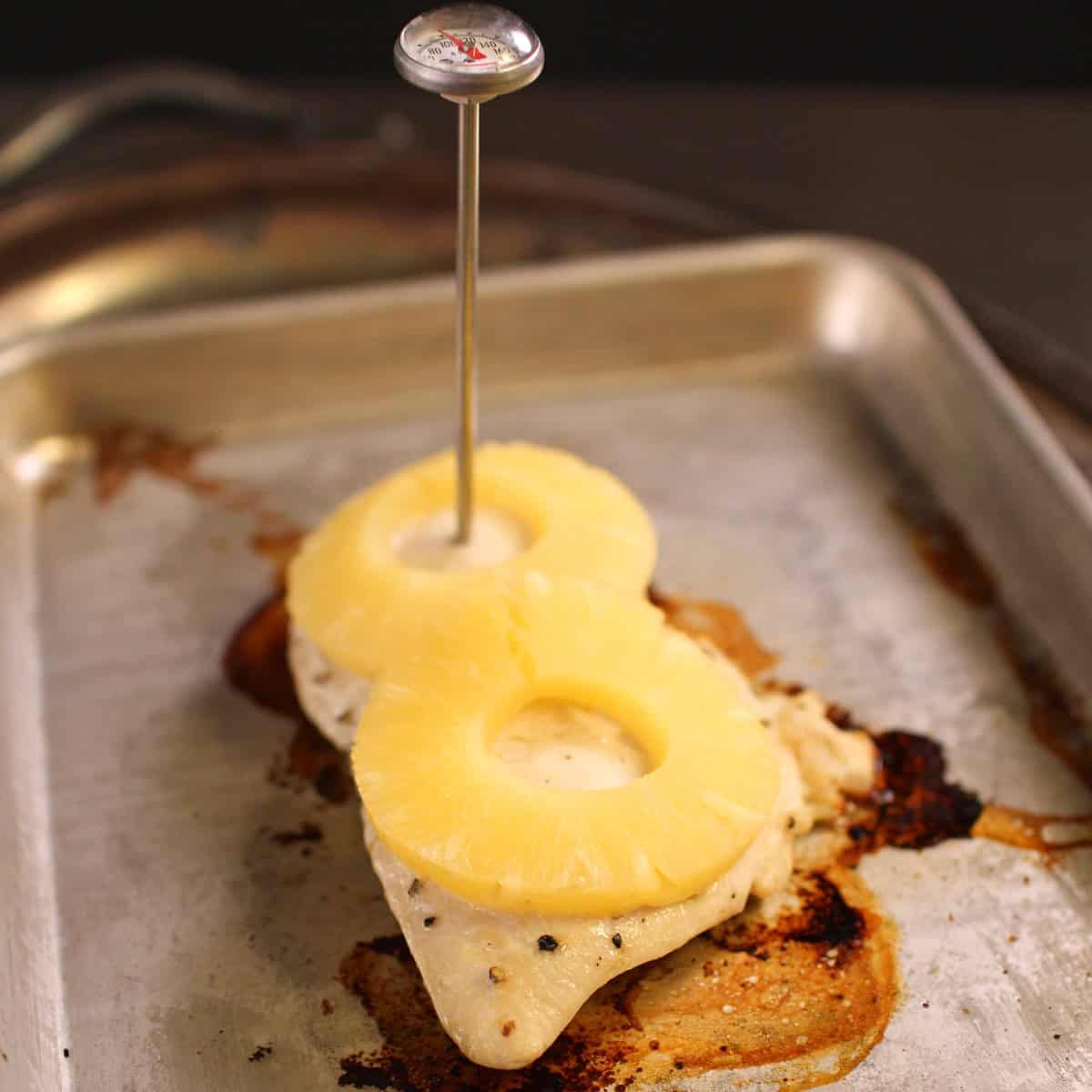 a broiled chicken breast on a baking sheet topped with pineapples.