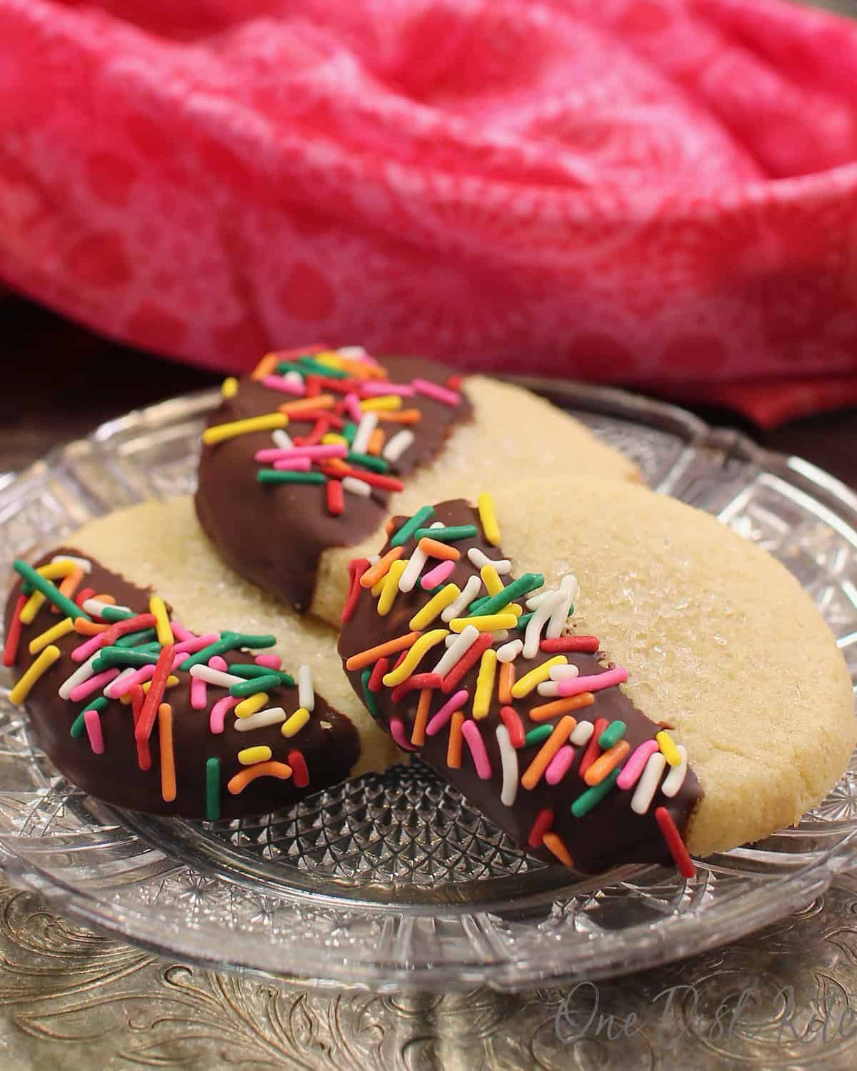 three chocolate dipped butter cookies on a plate next to a pink napkin.