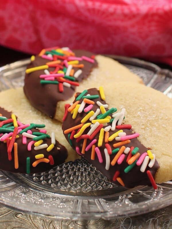 three chocolate dipped butter cookies on a plate next to a pink napkin.