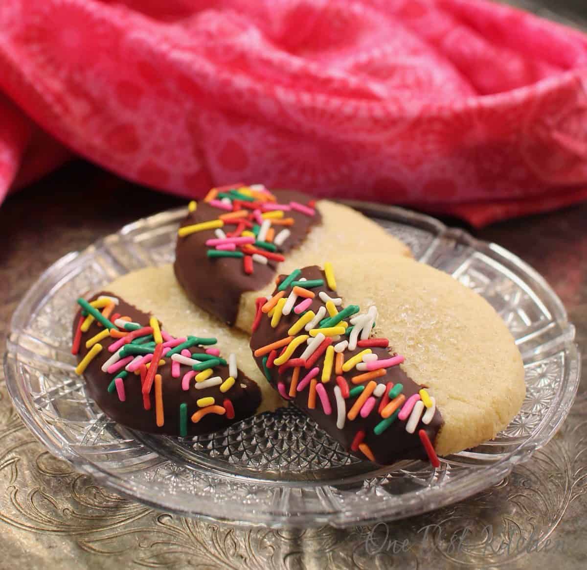 three chocolate dipped cookies on a plate next to a pink napkin.