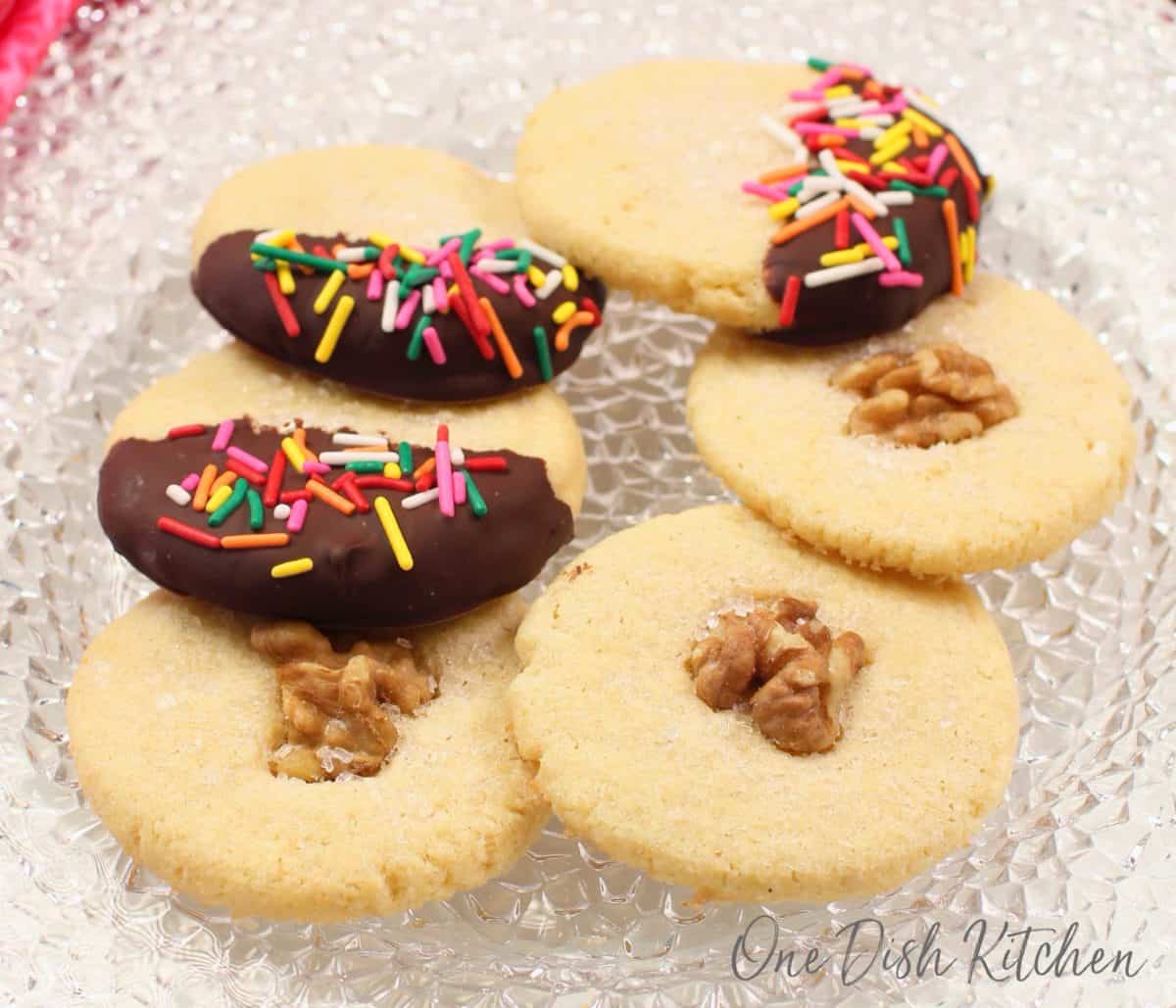 6 cookies on a clear plate; 3 cookies are dipped in chocolate and 3 have a nut in the center.