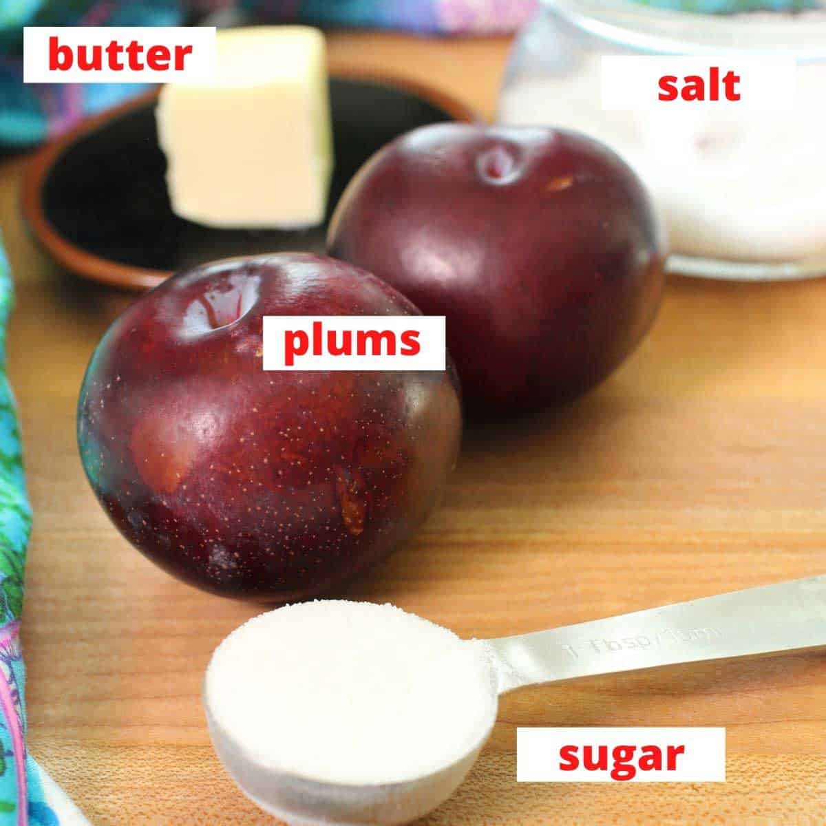 the ingredients for caramelized plums on a brown table including 2 plums, sugar, and butter.