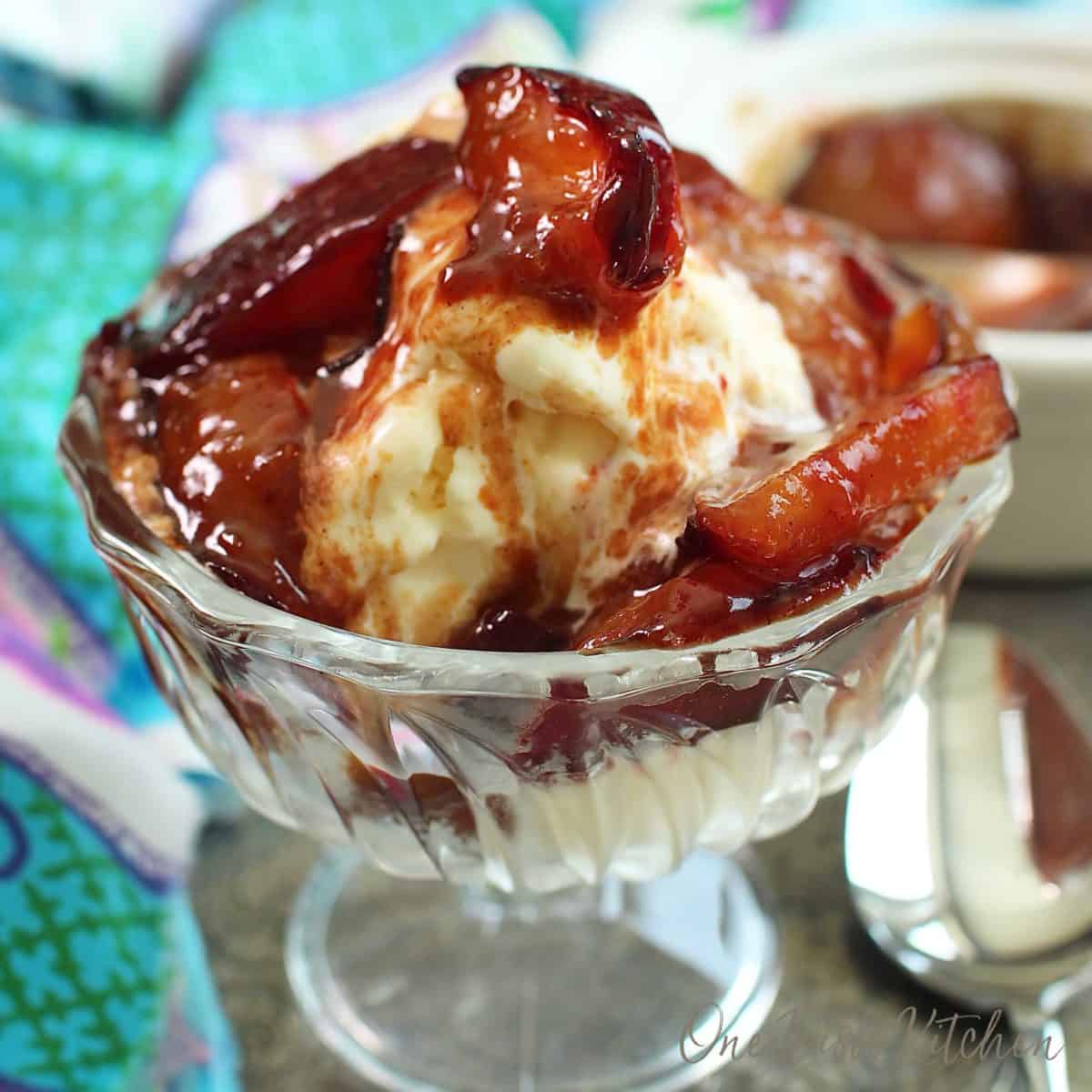 a bowl of ice cream topped with caramelized plums with a sugar sauce spooned over the top.