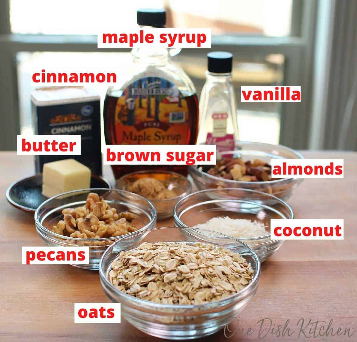 the ingredients needed to make butter pecan granola on a brown table next to an open window.