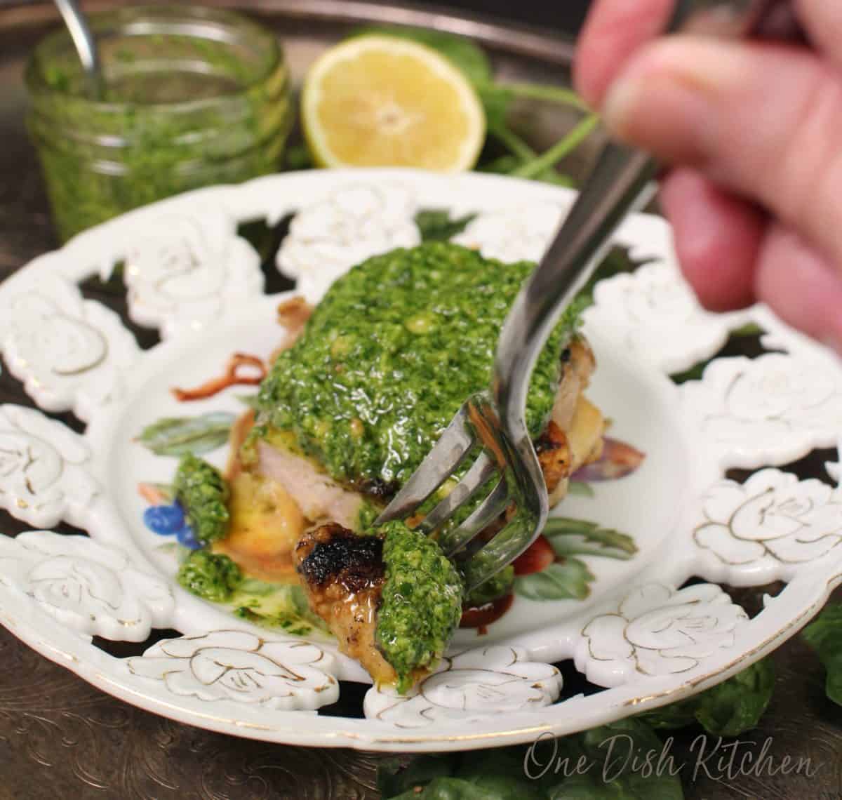 pesto chicken on a white plate with a fork filled with chicken.