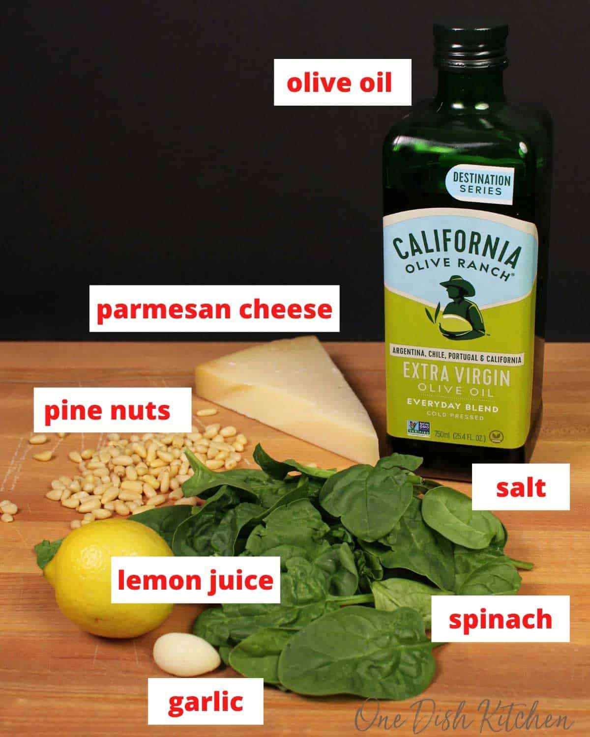 pine nuts, olive oil, lemons, cheese and spinach on a cutting board.