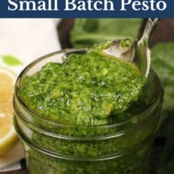 a jar of pesto on a table next to fresh spinach leaves.