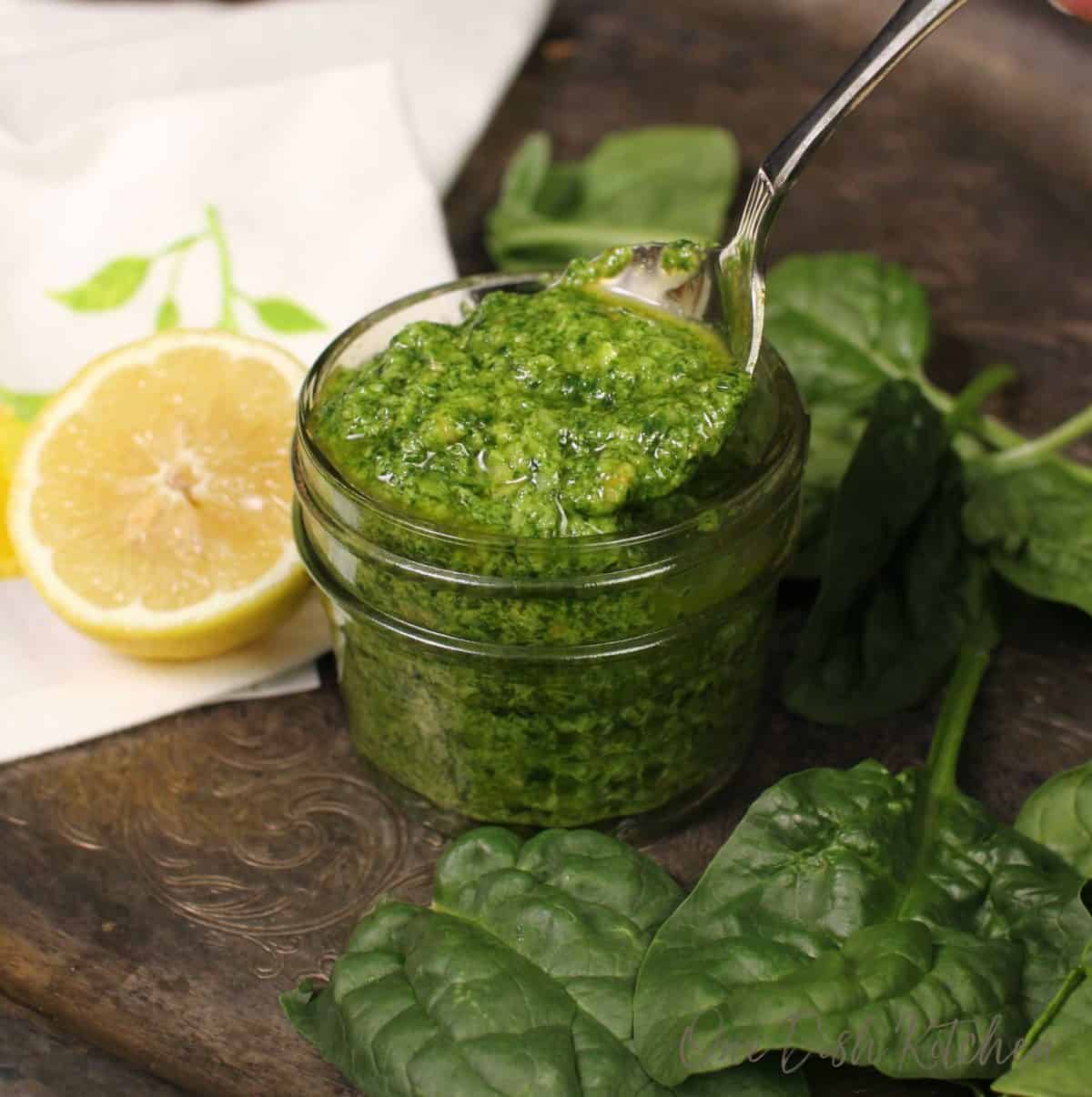 a jar of pesto with a spoon in the center coming out of the jar.