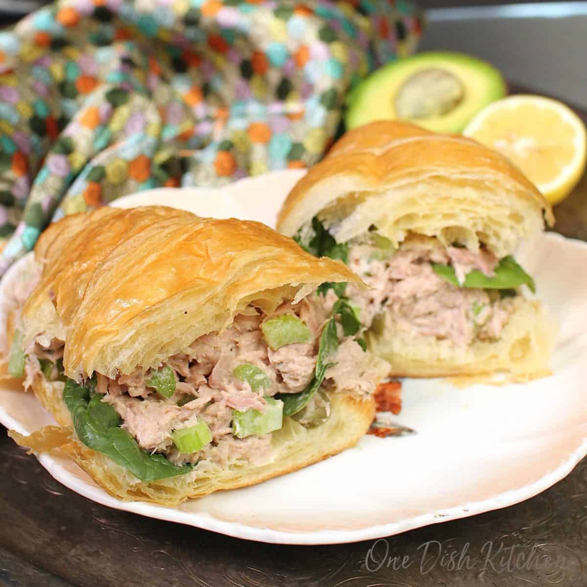 tuna salad on a croissant sliced in half on a white plate.