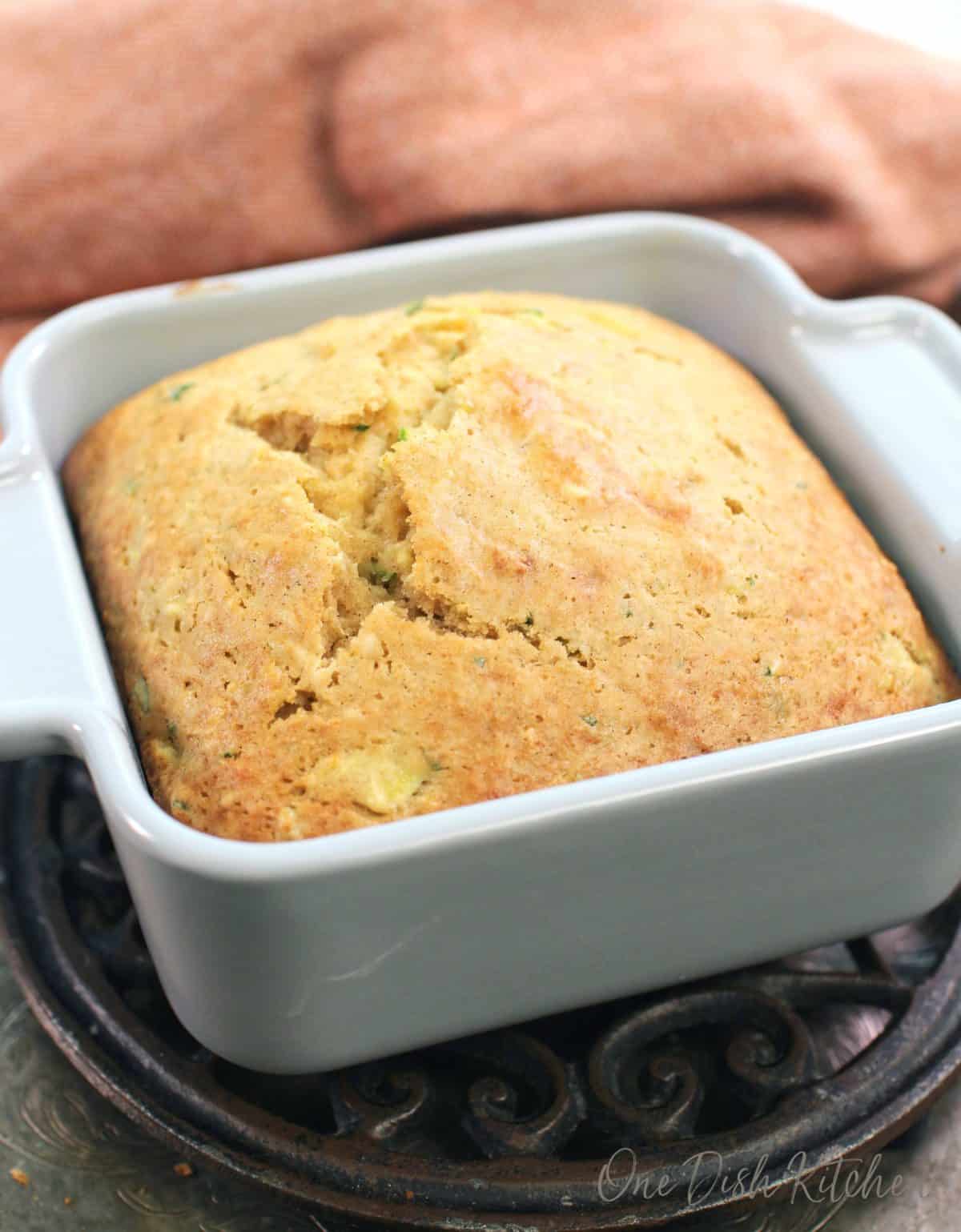 a small loaf of zucchini bread in square baking dish next to an orange napkin.