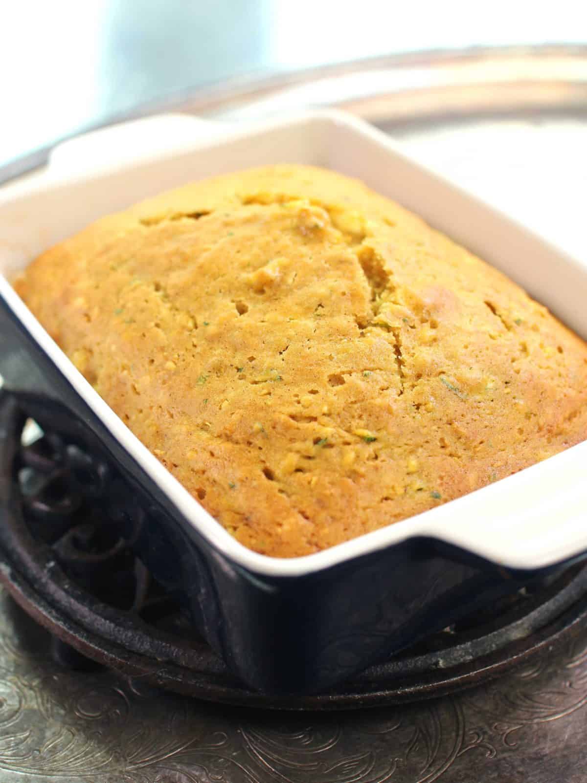 a loaf of zucchini bread baked in a rectangular blue baking dish on a metal trivet.