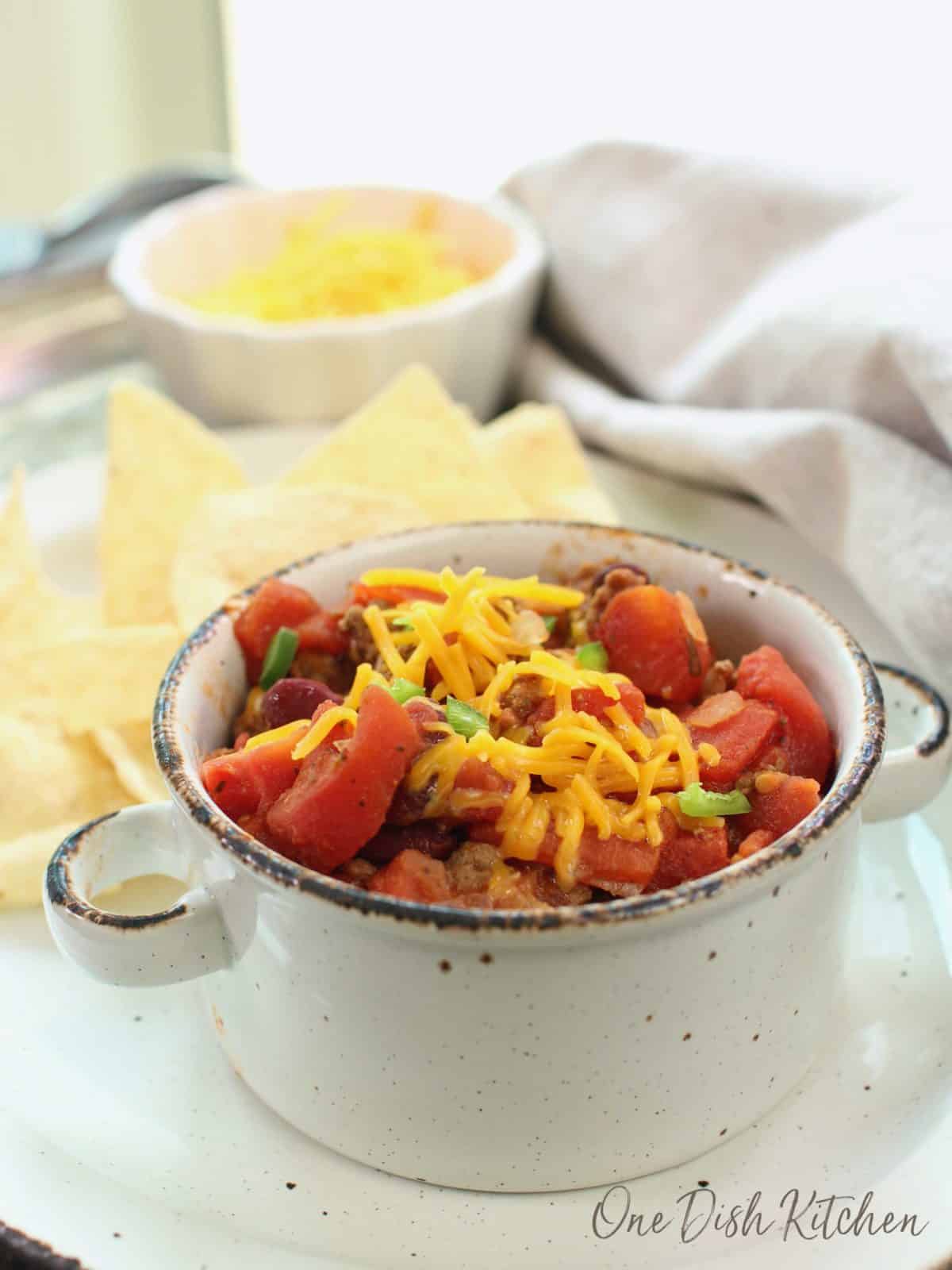 a white bowl filled with chili topped with shredded cheddar cheese.